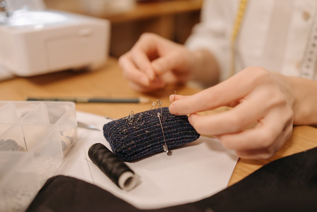Hands working on sewing fabric with pins and needles, close-up view.